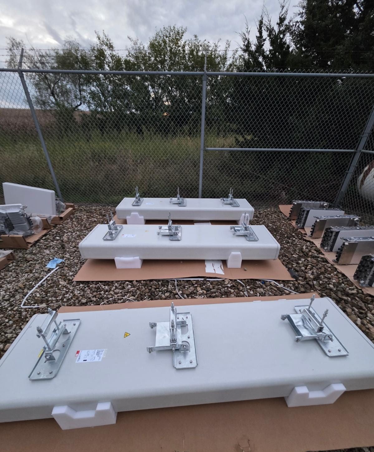 Two antennas with mounting brackets attached, laid on cardboard on the gravel compound, with radios staged behind them.